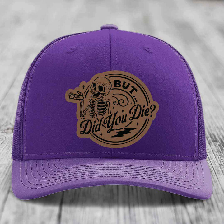 Purple trucker hat with a brown leatherette patch featuring a skeleton and the text &