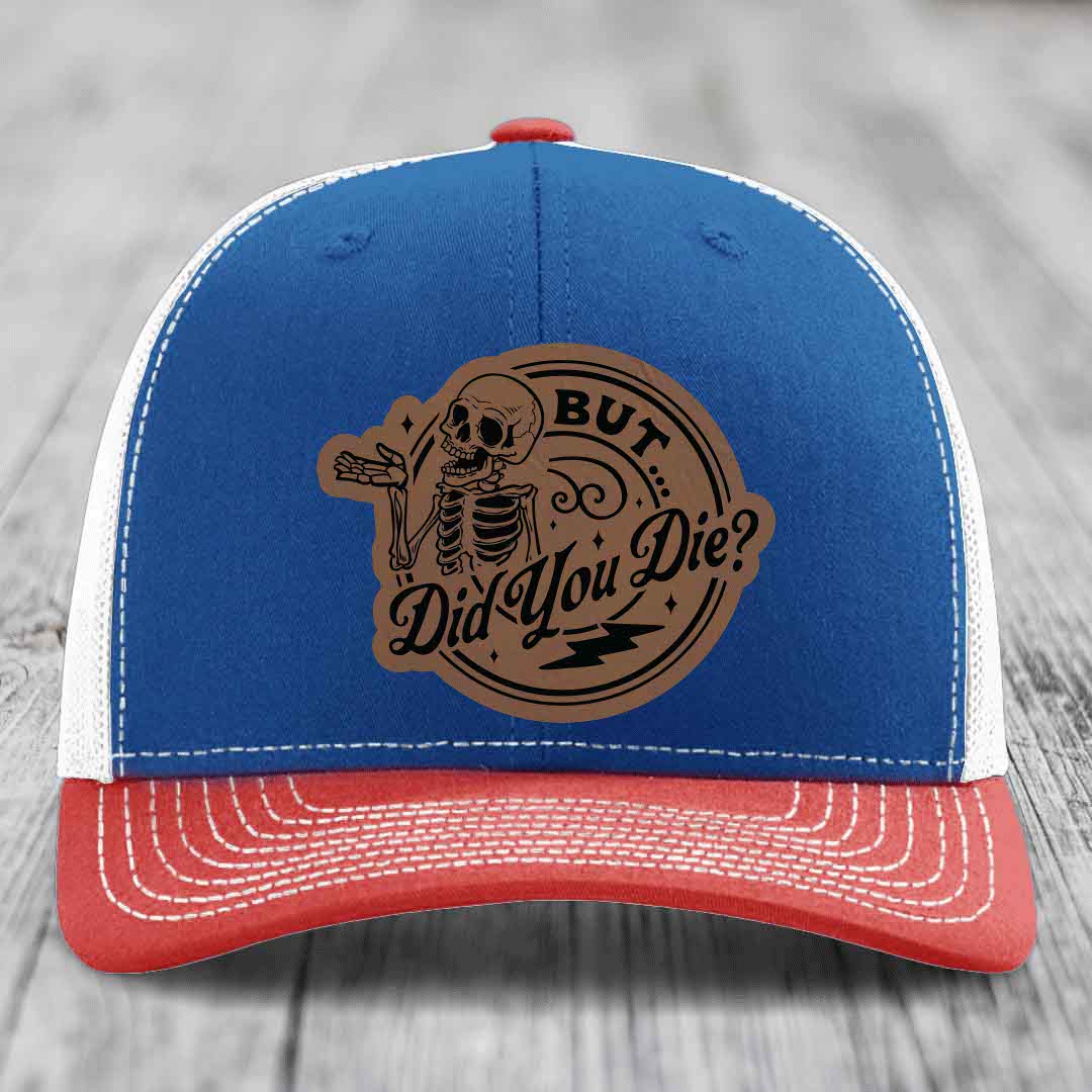Blue and red trucker hat with a brown leather patch featuring a skeleton and the text &