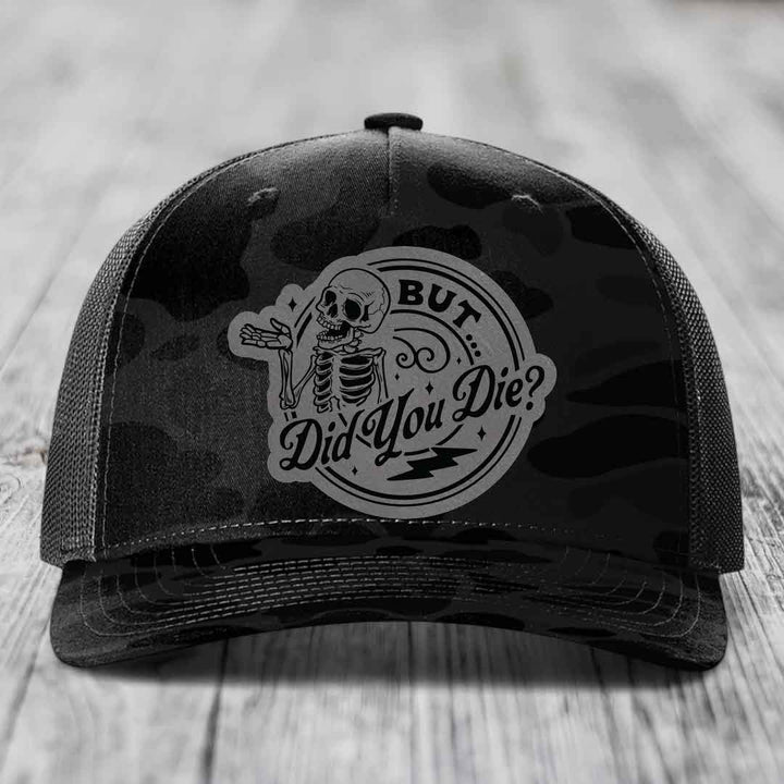 Black camouflage trucker hat with a grey skeleton patch that reads &