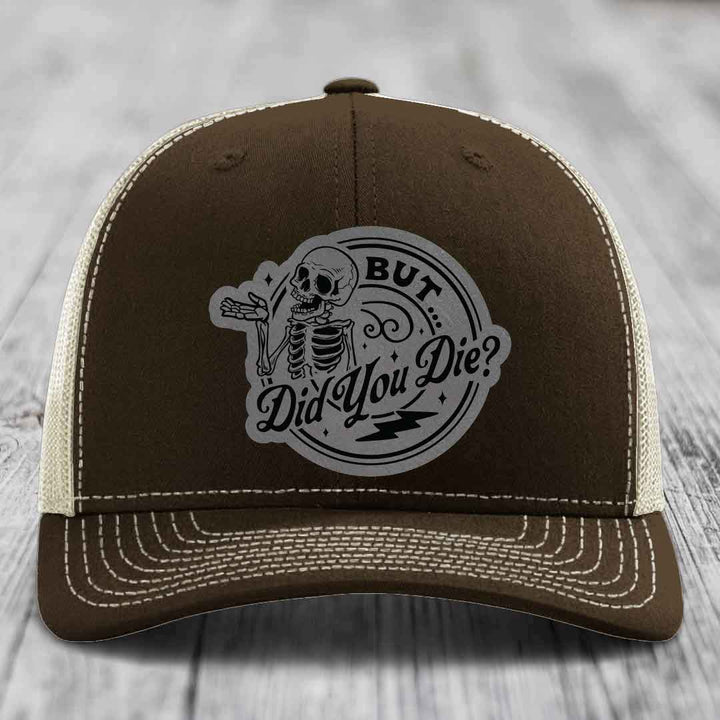 Brown trucker hat with white stitching and a skull patch that reads &