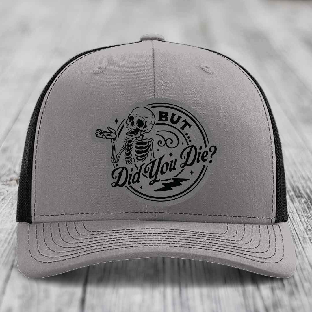 Grey trucker hat with black mesh back and embroidered skull patch reading &