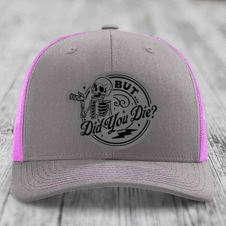 Grey trucker hat with pink mesh sides and black skull patch reading &