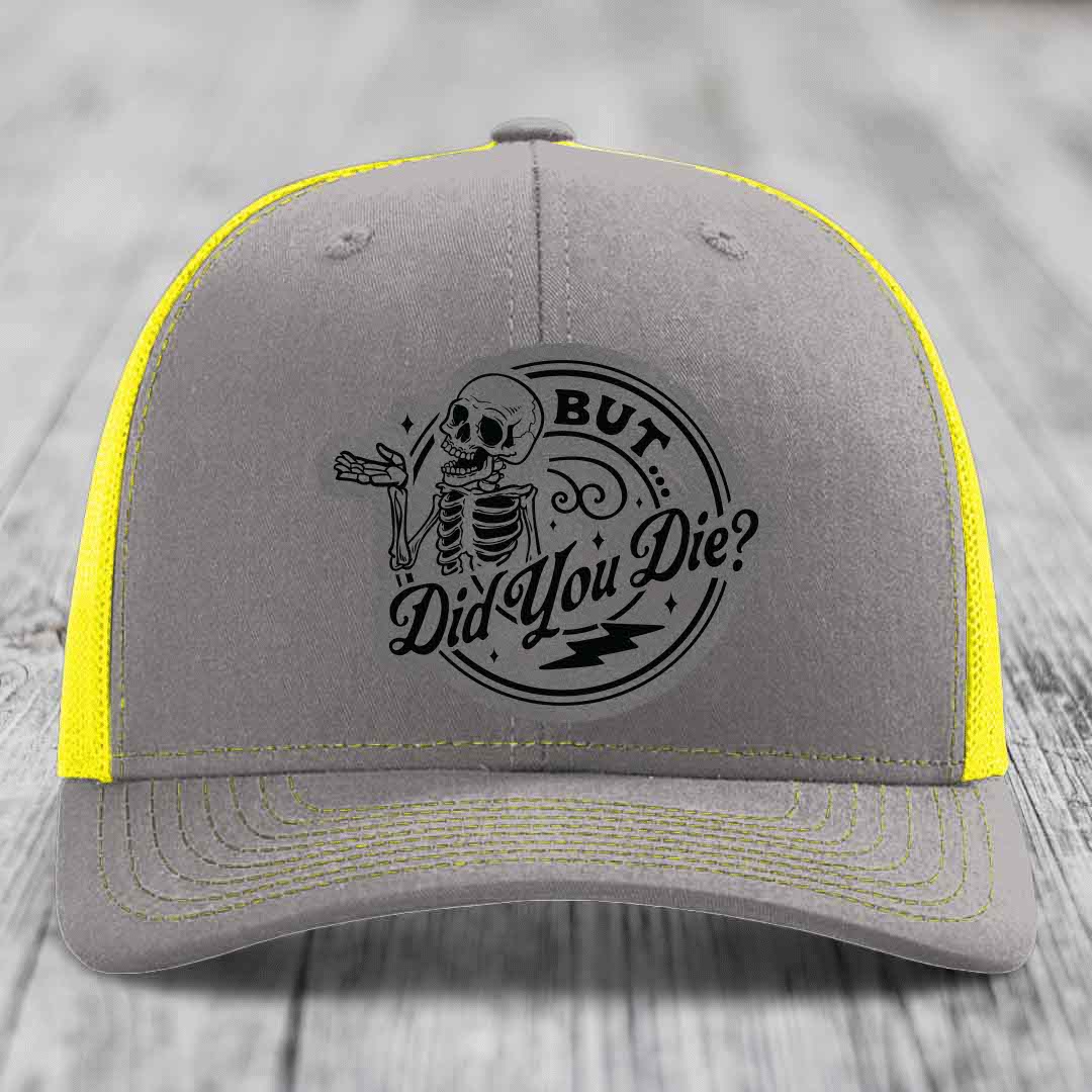 Grey trucker hat with yellow mesh sides and black embroidered skeleton patch reading &