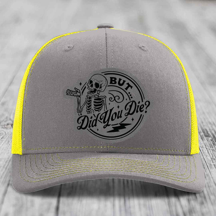 Grey trucker hat with yellow mesh sides and black embroidered skeleton patch reading &