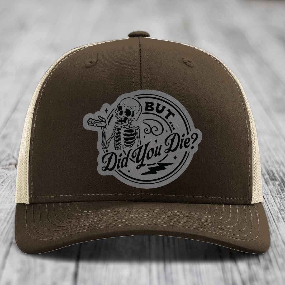Brown trucker hat with beige mesh back and a grey circular patch featuring a skeleton and the text &