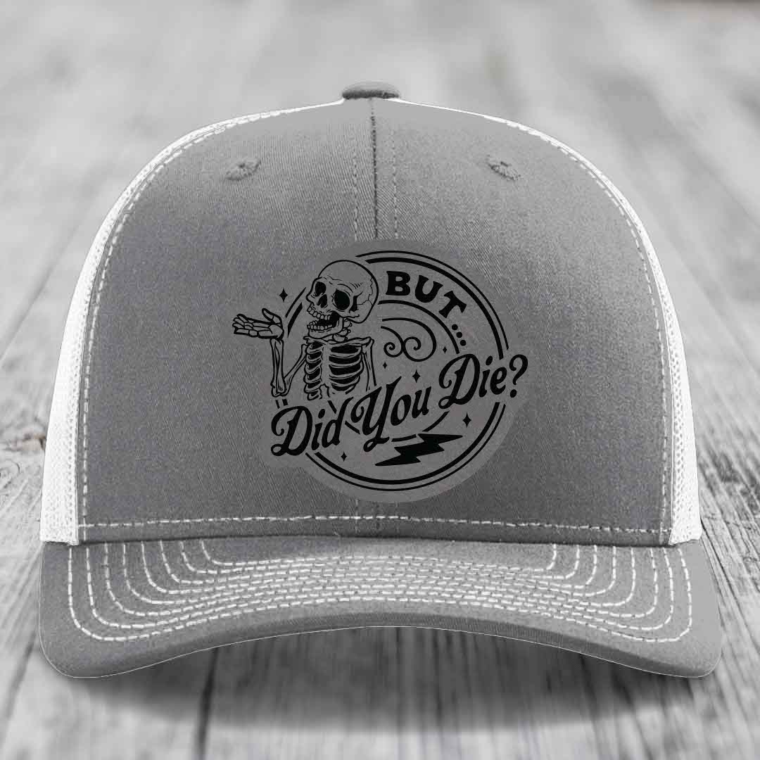 Grey trucker hat with white mesh back and embroidered skull patch reading &