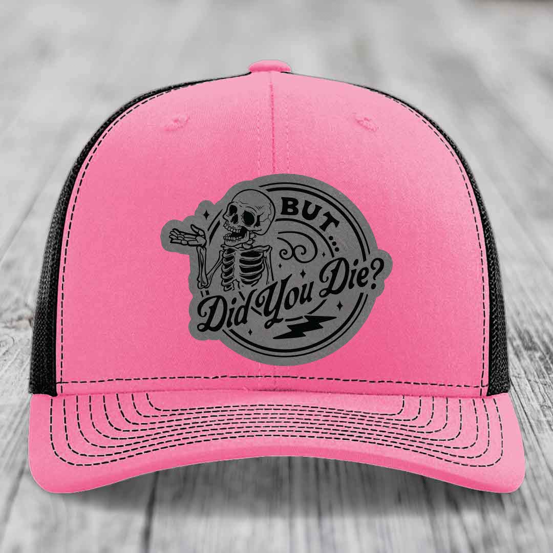 Pink trucker hat with black mesh back and gray circular patch featuring a skeleton and text &