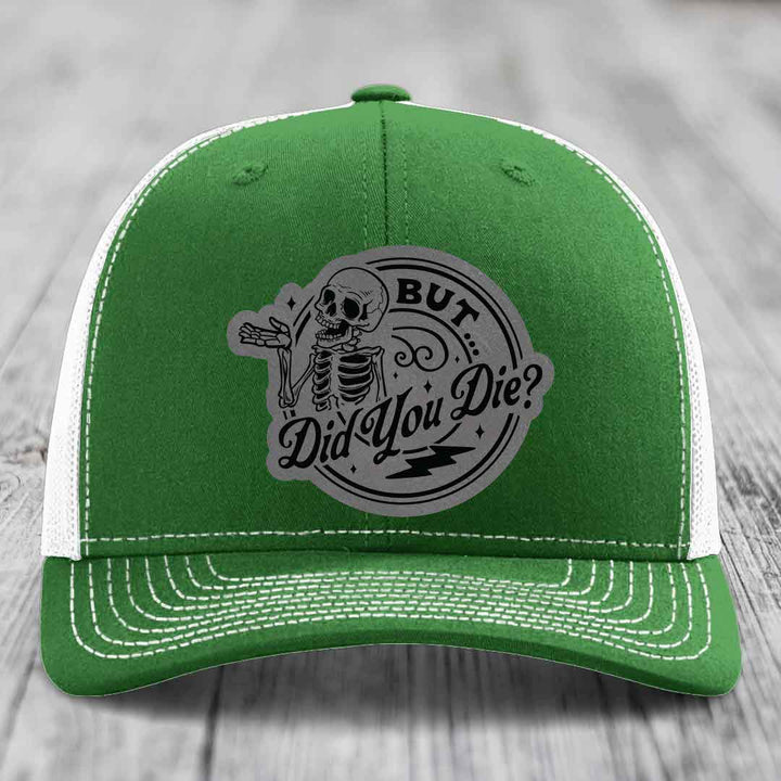 Green trucker hat with white mesh back and stitching, featuring a gray circular patch with a skeleton and text &