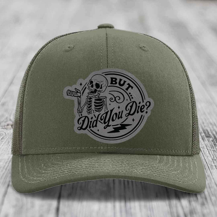 Olive green trucker hat with a circular patch featuring a skeleton and the text &