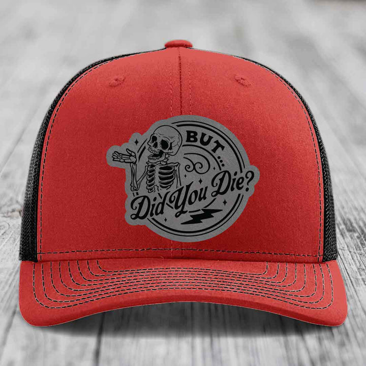Red trucker hat with black mesh back and gray circular patch featuring a skeleton and text &