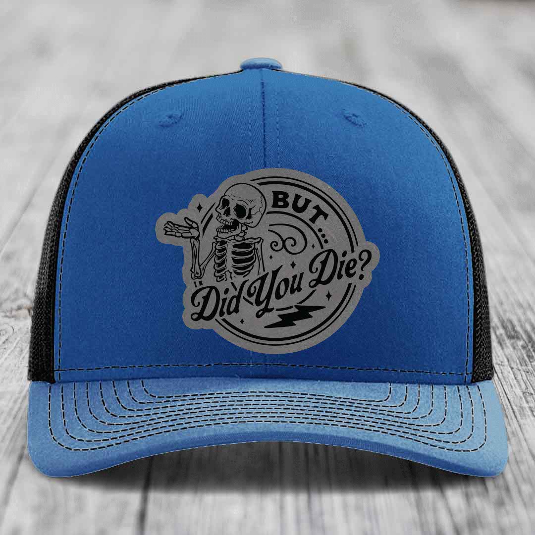Blue trucker hat with black mesh back and a gray circular patch featuring a skeleton and the text &