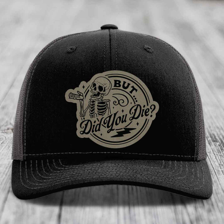 Black trucker hat with beige circular patch featuring a skeleton and text &