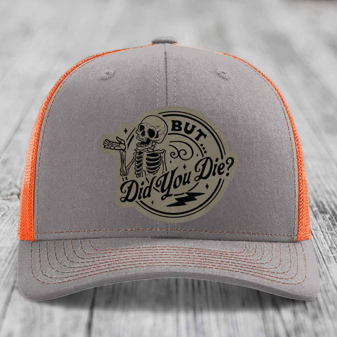 Grey trucker hat with orange mesh back and a skull patch that reads &