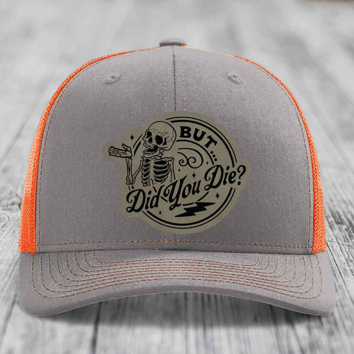 Grey trucker hat with orange mesh back and a skull patch that reads &