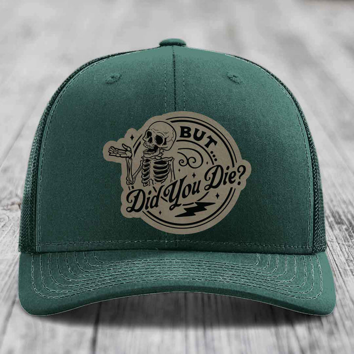 Dark green trucker hat with a beige circular patch featuring a skeleton and the text &