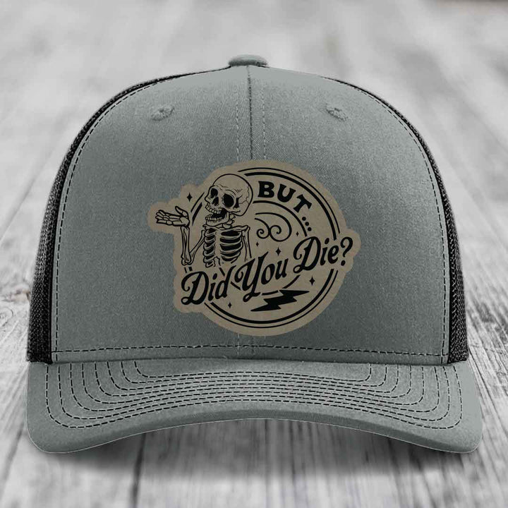 Grey trucker hat with a circular patch featuring a skeleton and the text &