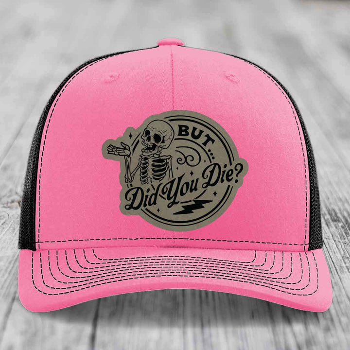 Pink trucker hat with black mesh back and a circular grey patch featuring a skeleton and text &