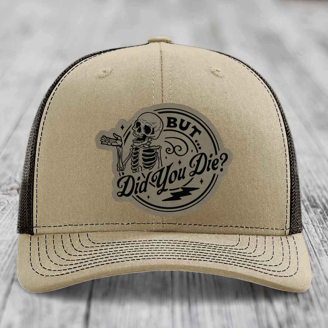 Beige trucker hat with black mesh back and a circular skull patch that reads &