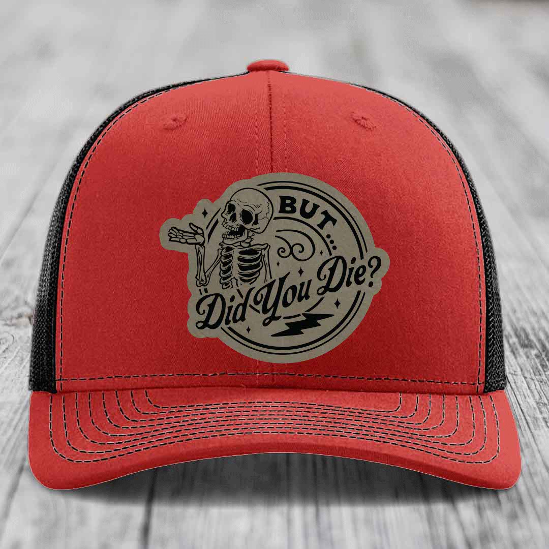 Red trucker hat with black mesh back and beige circular patch featuring a skeleton and text &