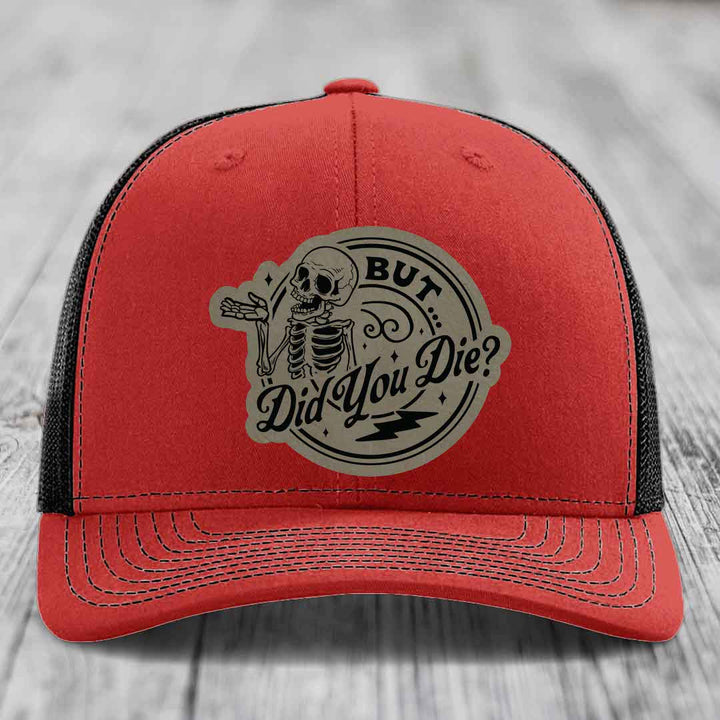 Red trucker hat with black mesh back and beige circular patch featuring a skeleton and text &