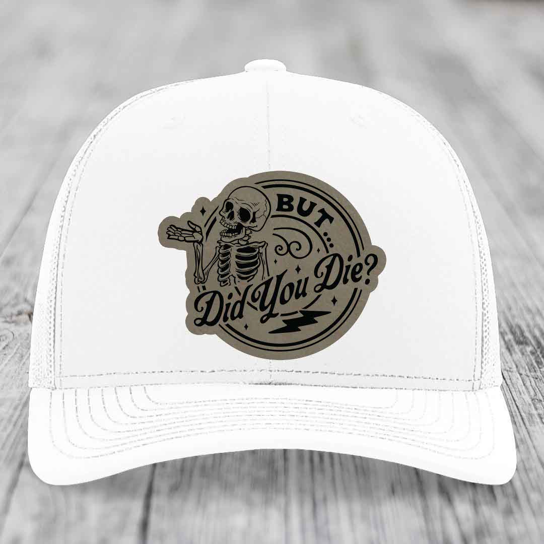 White trucker hat with a circular patch featuring a skeleton and the text &