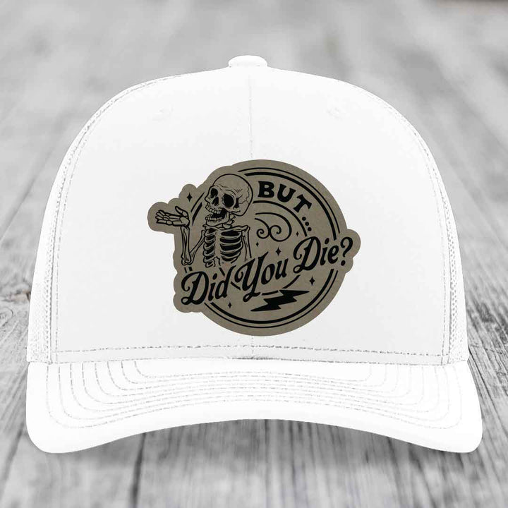 White trucker hat with a circular patch featuring a skeleton and the text &