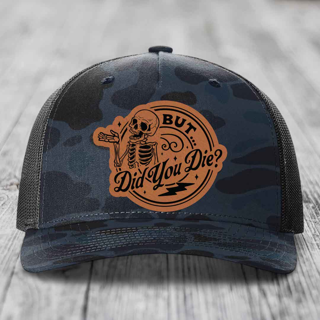 Camouflage trucker hat with brown leather patch featuring skeleton and text &