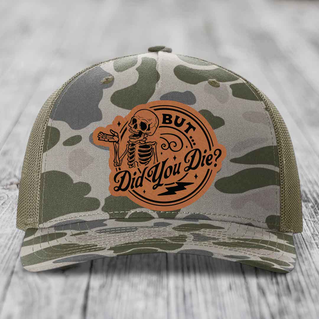Camouflage trucker hat with brown leather patch featuring skeleton and text &