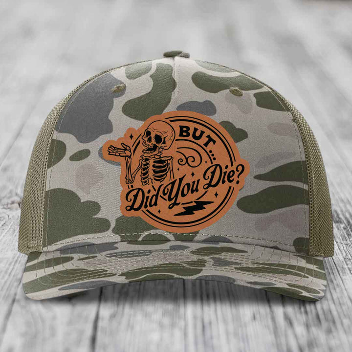 Camouflage trucker hat with brown leather patch featuring skeleton and text &