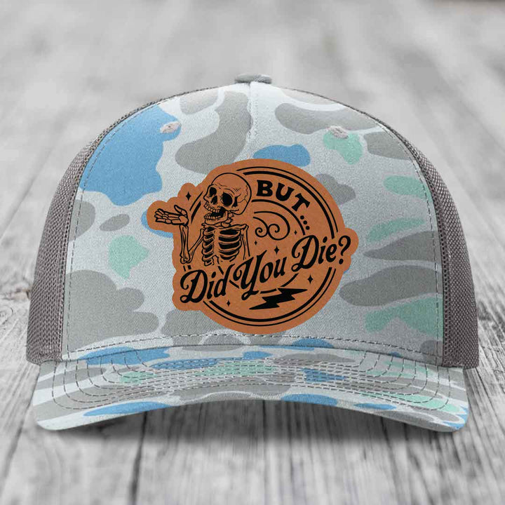 Camouflage trucker hat with brown leather patch featuring skeleton and text &