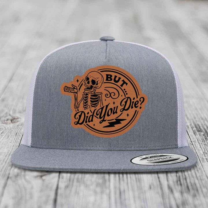 Grey trucker hat with brown leather patch featuring a skeleton and text &