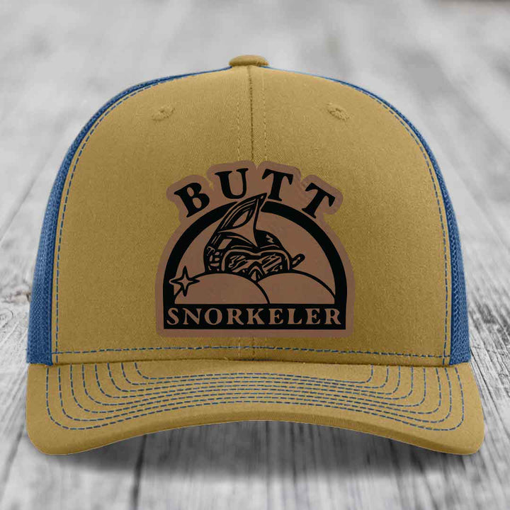 Tan trucker hat with blue mesh back and brown leather patch reading &