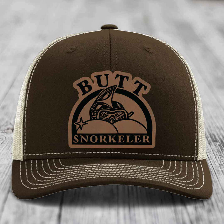 Brown trucker hat with beige mesh back and white stitching, featuring a &