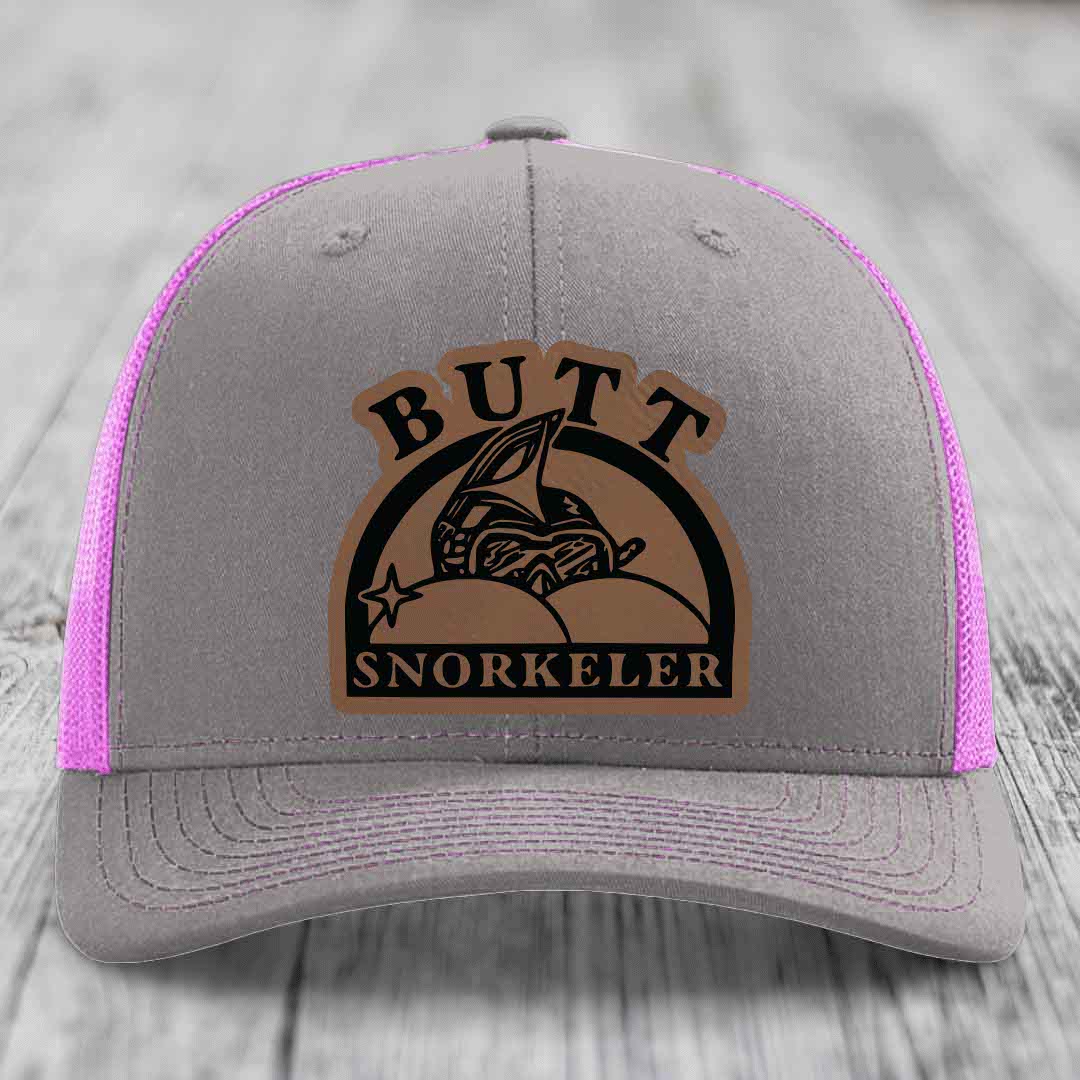 Grey trucker hat with pink mesh sides and a brown leather patch reading &