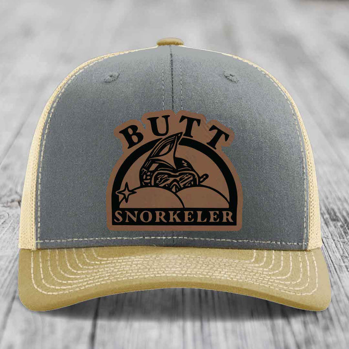 Grey and beige trucker hat with a brown leather patch reading &