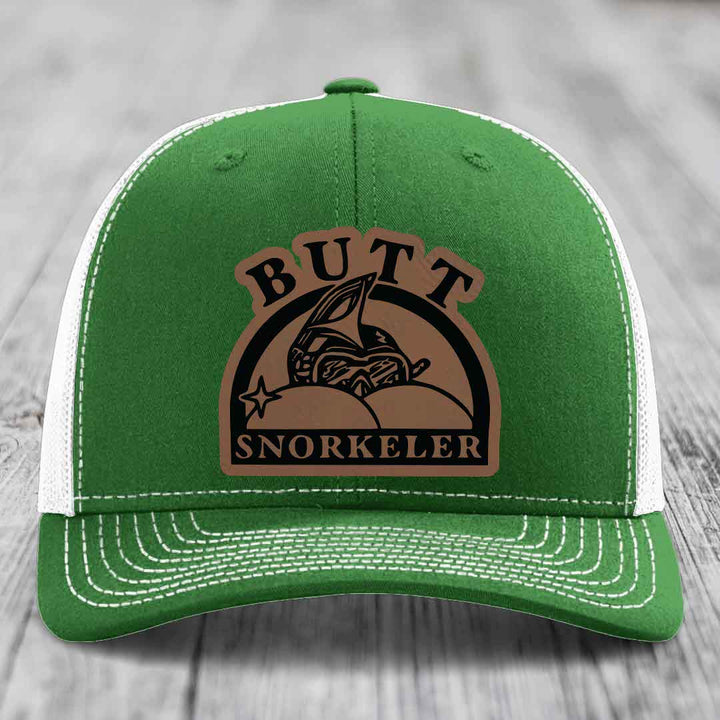 Green trucker hat with white mesh back and brown leather patch reading &