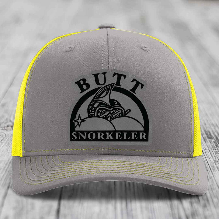 Grey trucker hat with yellow mesh sides and stitching, featuring a black &