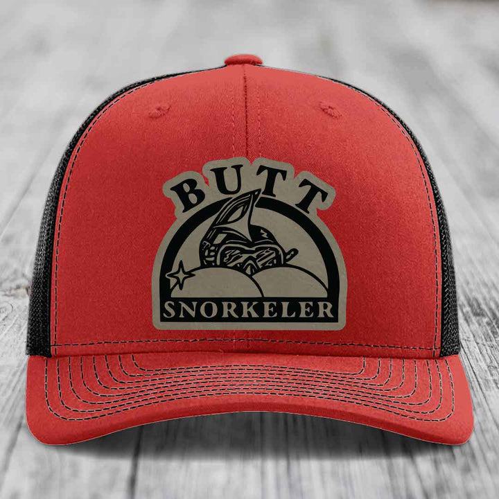 Red trucker hat with black mesh back and a beige leatherette patch reading &