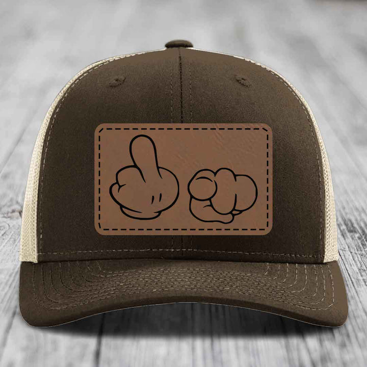 Brown trucker hat with beige mesh back and a brown leather patch featuring cartoon hands making rude gestures.