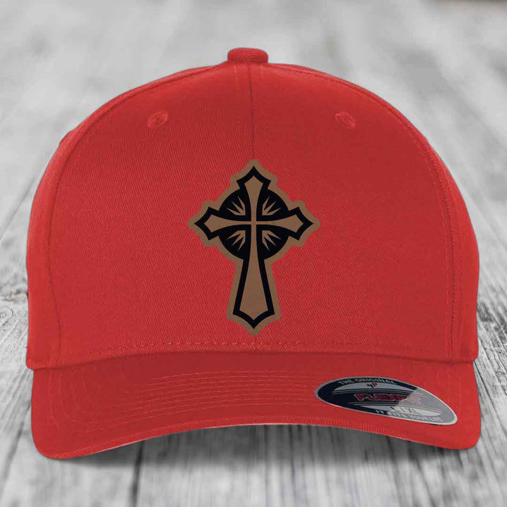 Red baseball cap with a cross patch featuring black and tan details, branded Flexfit label on brim.