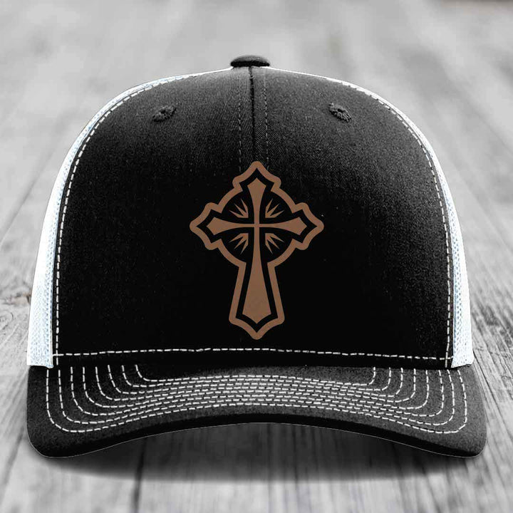 Black trucker hat with brown cross patch and white stitching on front panel.