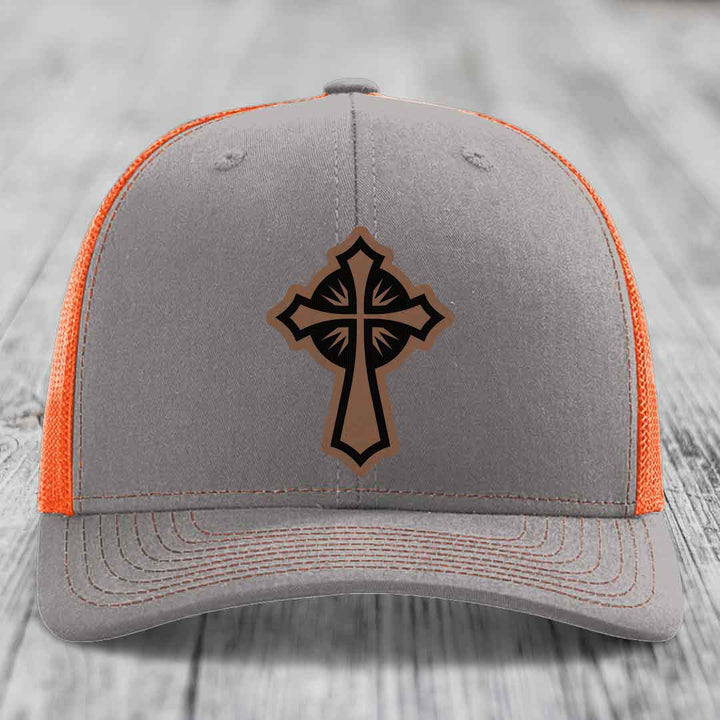 Grey trucker hat with orange mesh back and black cross leather patch on front.
