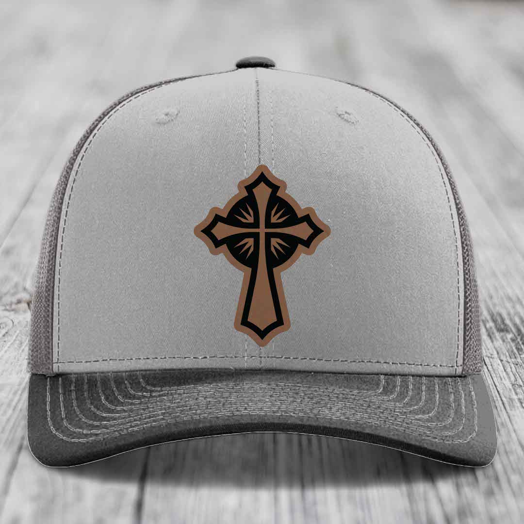 Grey trucker hat with a brown and black leatherette cross patch on the front.