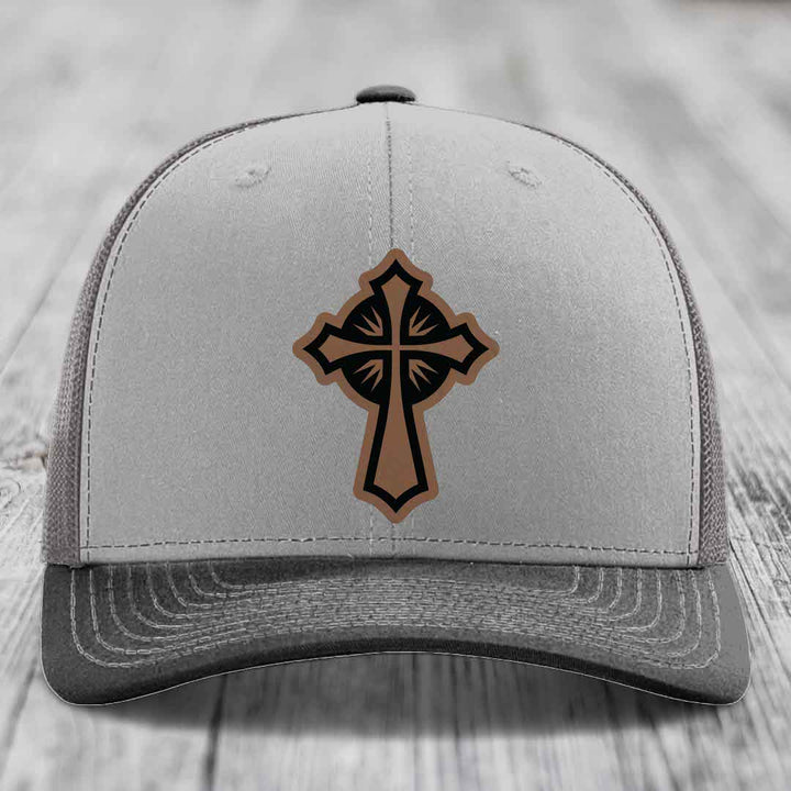 Grey trucker hat with a brown and black leatherette cross patch on the front.
