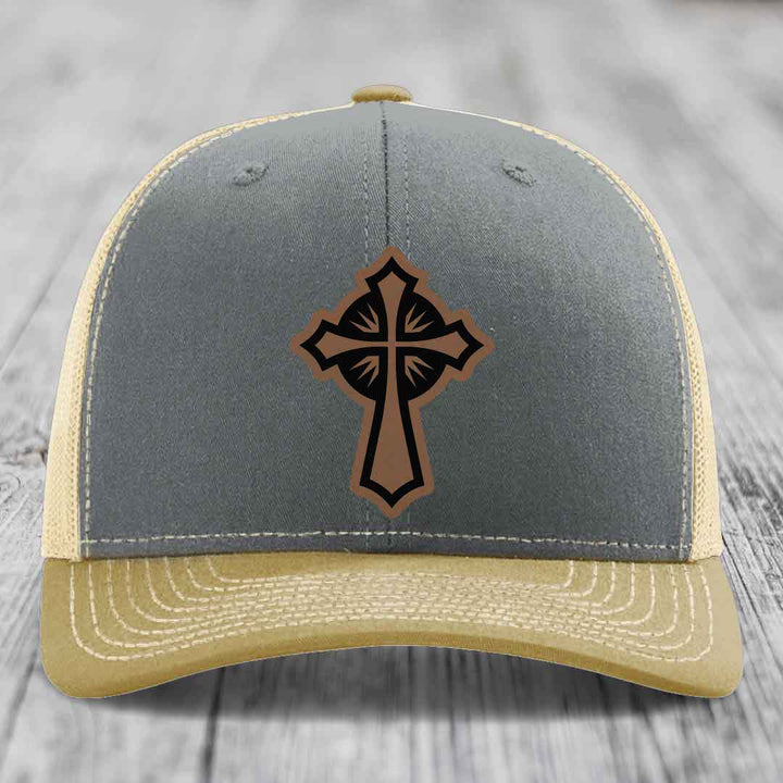 Grey and beige trucker hat with a brown leather cross patch on front.