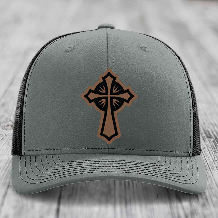 Grey trucker hat with a brown and black leather cross patch on front.