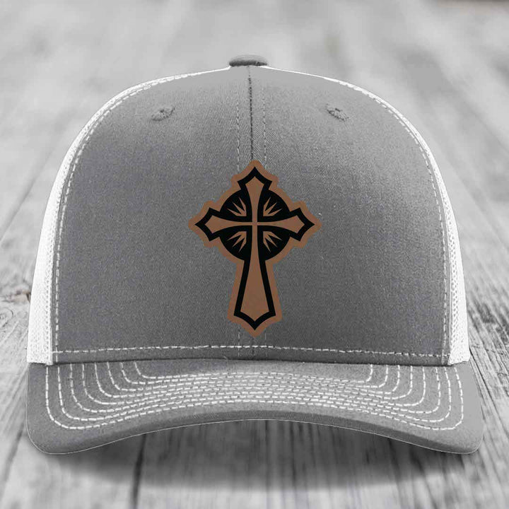 Grey trucker hat with brown and black cross leather patch on front.