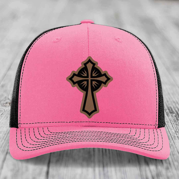 Pink trucker hat with black mesh back and a brown cross leather patch on front.