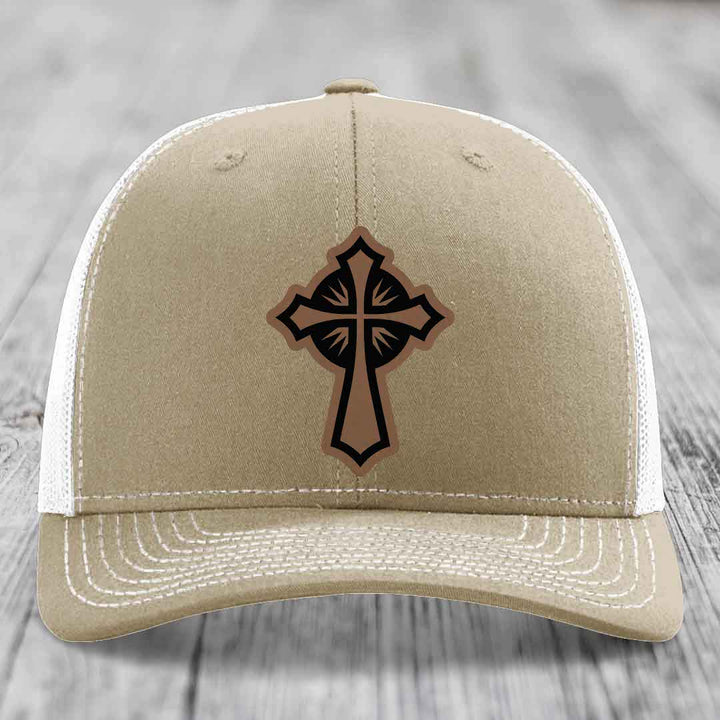 Tan trucker hat with black and brown cross leather patch on front.
