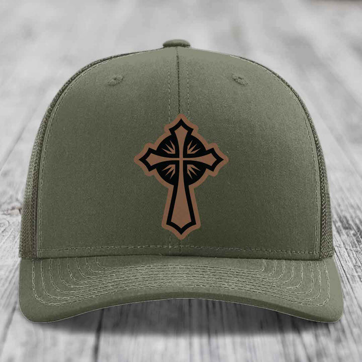 Olive green trucker hat with a brown and black cross leather patch on front.